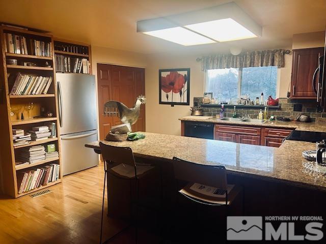 kitchen with stainless steel refrigerator, dishwasher, light stone counters, kitchen peninsula, and light wood-type flooring