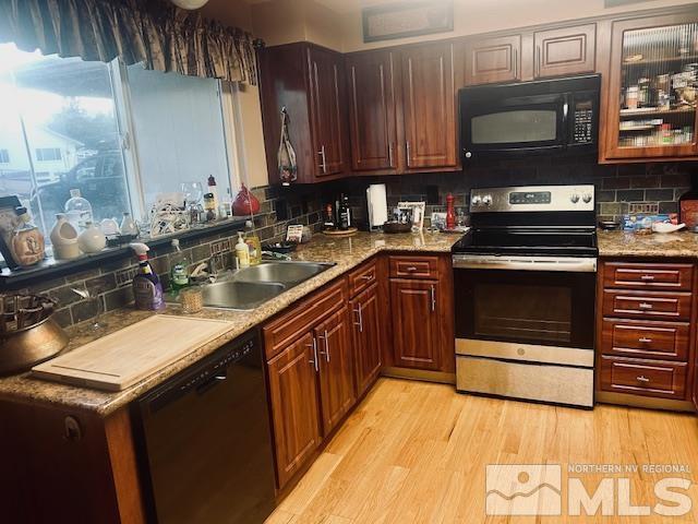 kitchen featuring black appliances, light stone counters, light wood-type flooring, and sink