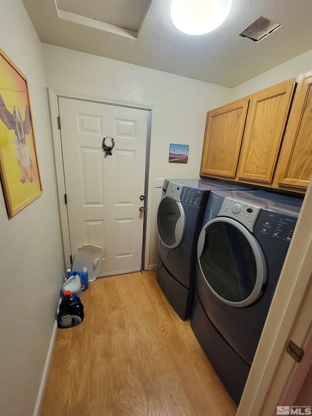 laundry room featuring cabinets, washing machine and dryer, a textured ceiling, and light hardwood / wood-style flooring