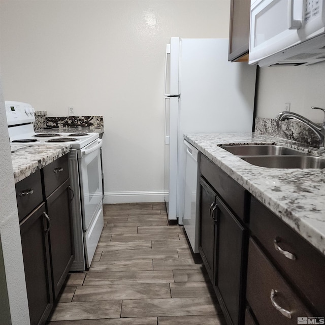 kitchen featuring dark brown cabinets, light stone counters, white appliances, and sink