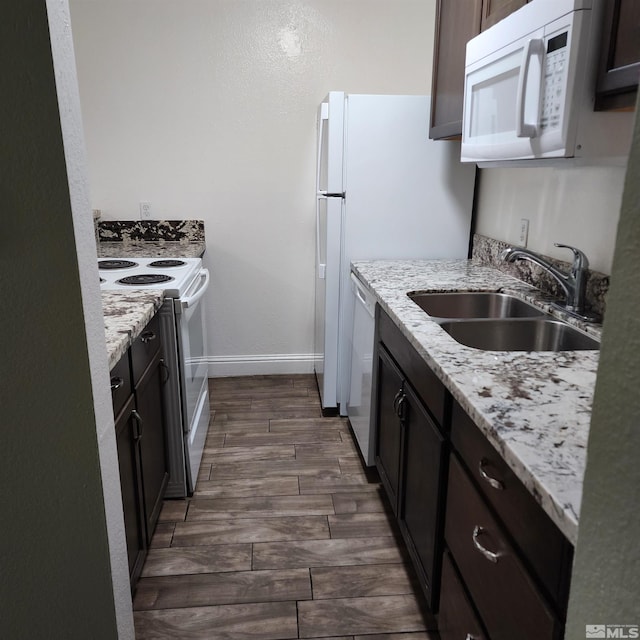 kitchen featuring dark brown cabinetry, sink, dark wood-type flooring, light stone counters, and white appliances