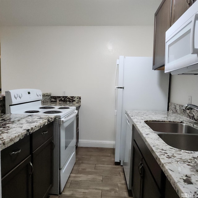 kitchen featuring light stone counters, dark brown cabinets, white appliances, dark wood-type flooring, and sink