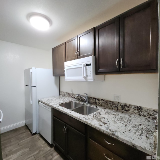 kitchen with white appliances, sink, light stone countertops, dark brown cabinets, and dark hardwood / wood-style flooring