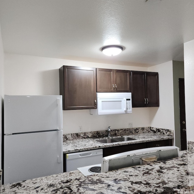 kitchen featuring light stone counters, a textured ceiling, white appliances, dark brown cabinetry, and sink