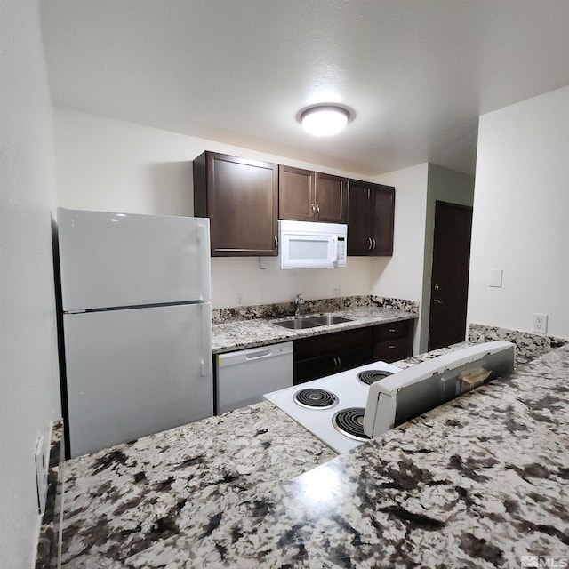 kitchen with light stone countertops, dark brown cabinetry, white appliances, and sink