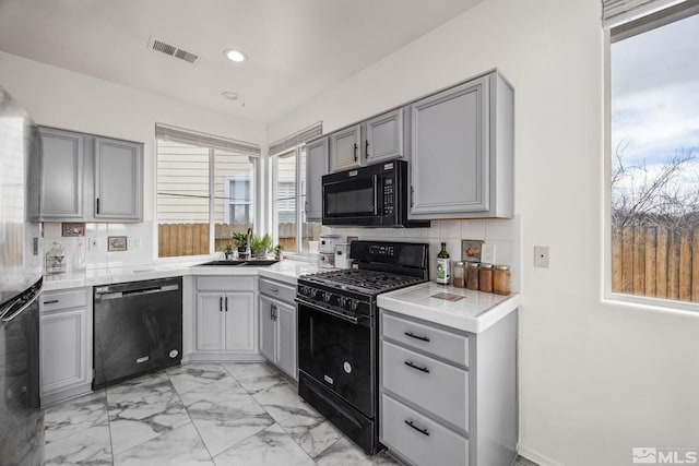 kitchen featuring tasteful backsplash, sink, black appliances, tile countertops, and gray cabinets