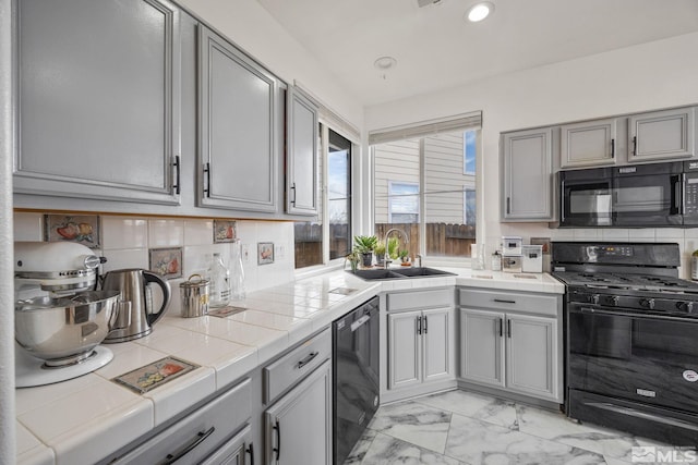 kitchen with sink, backsplash, tile countertops, gray cabinets, and black appliances