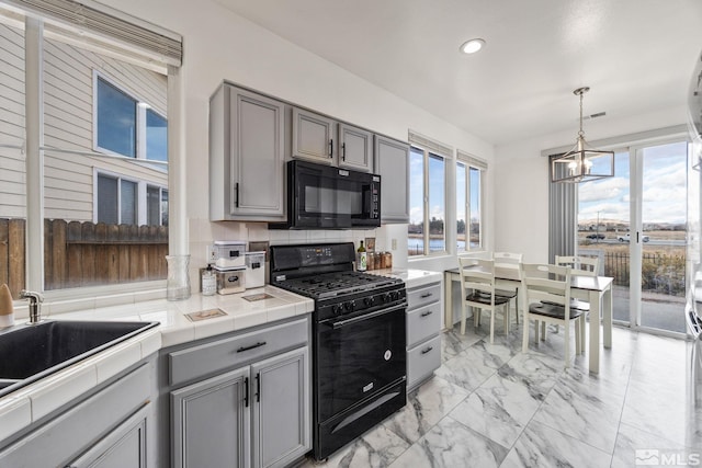 kitchen with decorative backsplash, gray cabinetry, black appliances, tile counters, and hanging light fixtures