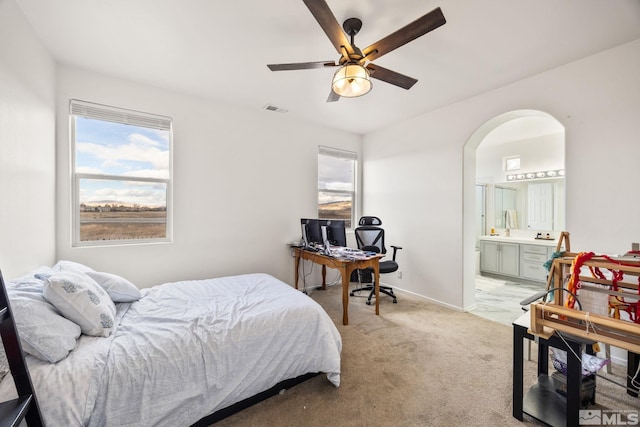 bedroom featuring light carpet, ensuite bathroom, and ceiling fan