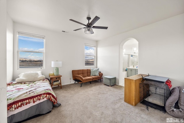 carpeted bedroom with multiple windows, ceiling fan, and ensuite bath