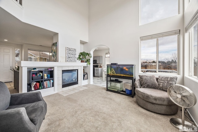 living room with carpet flooring, a towering ceiling, and a tile fireplace