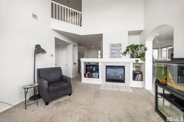 living room with a tile fireplace, light carpet, and a towering ceiling