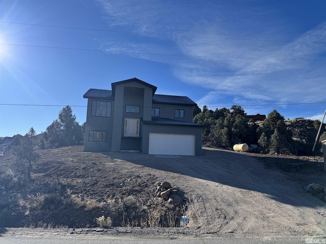 view of front of property featuring an attached garage, dirt driveway, and stucco siding