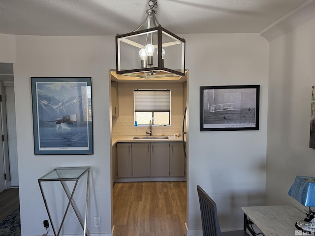 kitchen with sink, hanging light fixtures, light hardwood / wood-style flooring, decorative backsplash, and a chandelier