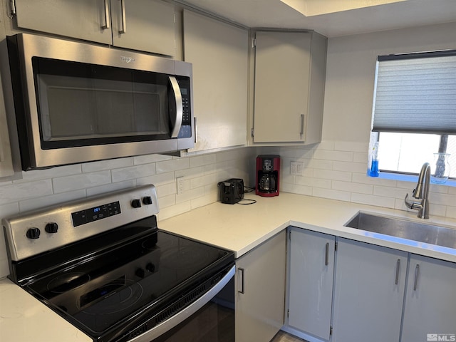 kitchen featuring appliances with stainless steel finishes, gray cabinets, tasteful backsplash, and sink