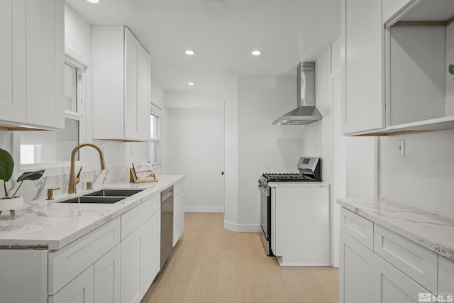 kitchen with white cabinets, wall chimney range hood, sink, light wood-type flooring, and stainless steel appliances