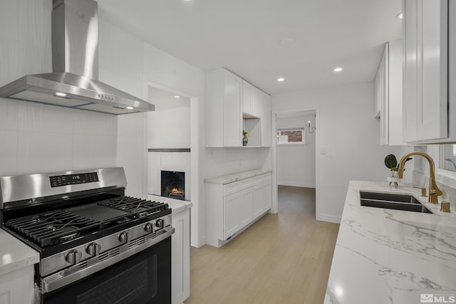 kitchen featuring white cabinetry, stainless steel gas range oven, wall chimney exhaust hood, and sink