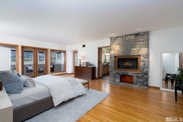 bedroom featuring wood-type flooring, access to outside, a stone fireplace, and ensuite bathroom