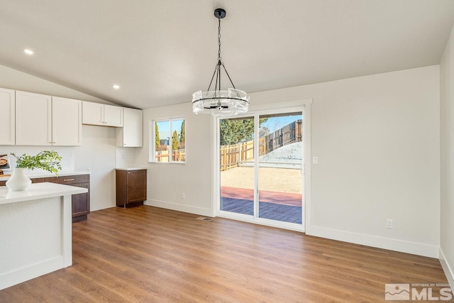 unfurnished dining area featuring a notable chandelier, lofted ceiling, and light hardwood / wood-style flooring