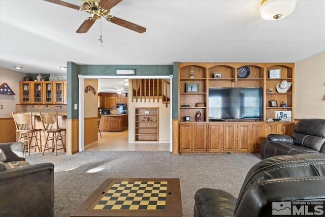 living room with bar, light carpet, ceiling fan, and wood walls