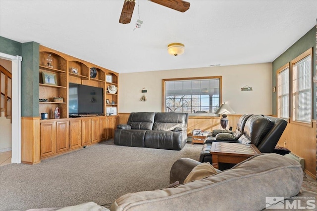 living room with plenty of natural light, wood walls, light colored carpet, and ceiling fan