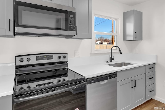 kitchen with hardwood / wood-style floors, gray cabinets, sink, and appliances with stainless steel finishes