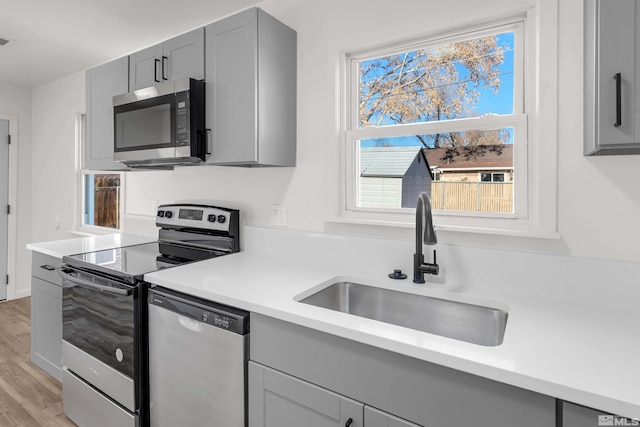 kitchen with gray cabinets, light wood-type flooring, sink, and appliances with stainless steel finishes