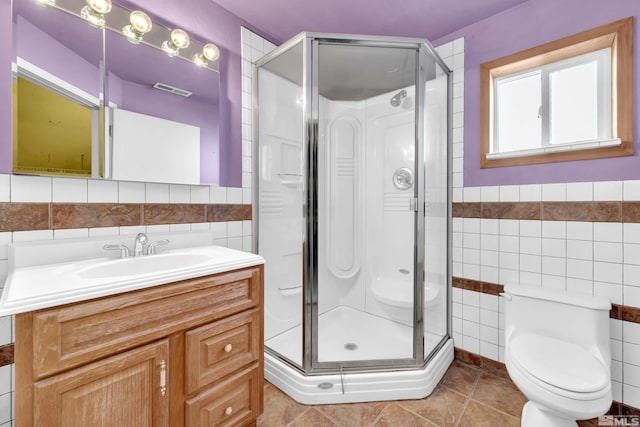 bathroom with vanity, tile patterned flooring, toilet, tile walls, and a shower with shower door