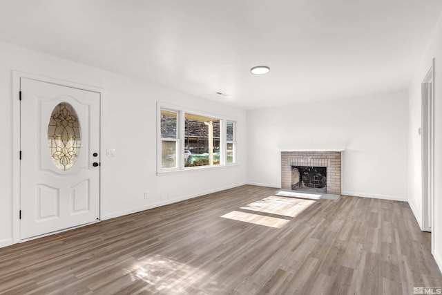 unfurnished living room with wood-type flooring and a brick fireplace