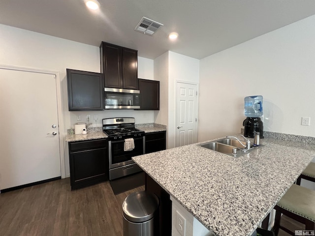 kitchen with dark wood-type flooring, stainless steel appliances, light stone counters, kitchen peninsula, and a kitchen bar