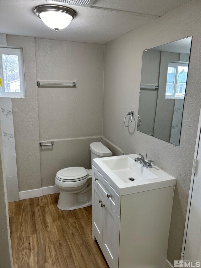 bathroom with wood-type flooring, vanity, toilet, and a healthy amount of sunlight