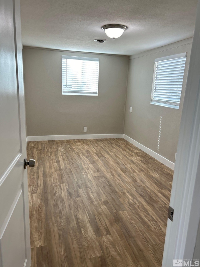 unfurnished room featuring a textured ceiling, dark hardwood / wood-style flooring, and plenty of natural light