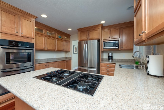 kitchen with sink, stainless steel appliances, light stone counters, a textured ceiling, and a breakfast bar area