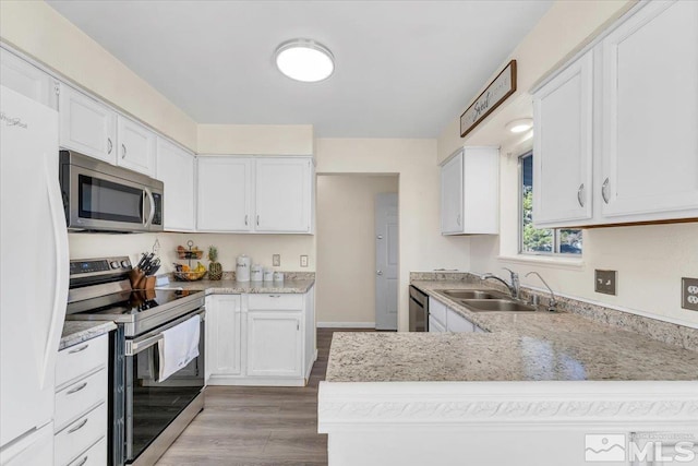 kitchen featuring kitchen peninsula, appliances with stainless steel finishes, light wood-type flooring, sink, and white cabinetry