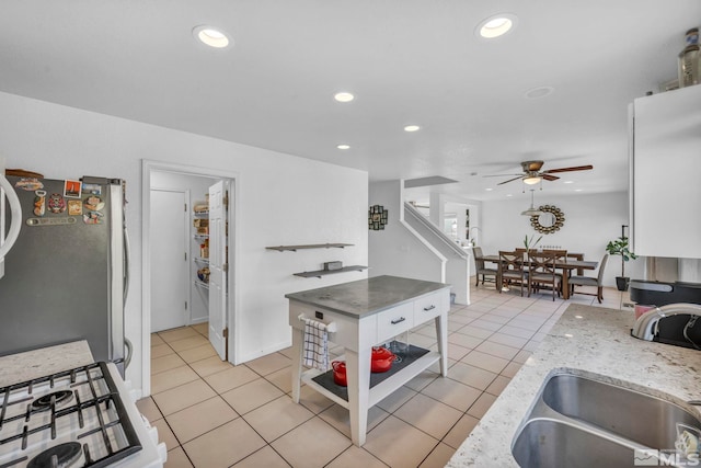 kitchen featuring sink, ceiling fan, light tile patterned flooring, white cabinetry, and stainless steel refrigerator