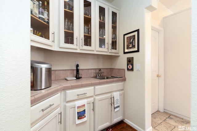 bar with white cabinetry, tile counters, and sink