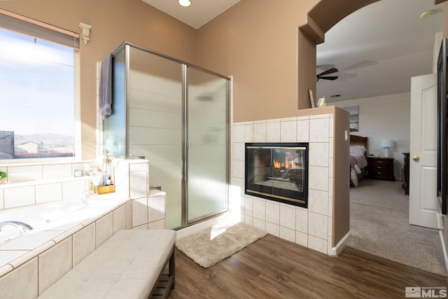 bathroom with ceiling fan, a fireplace, plus walk in shower, and hardwood / wood-style flooring