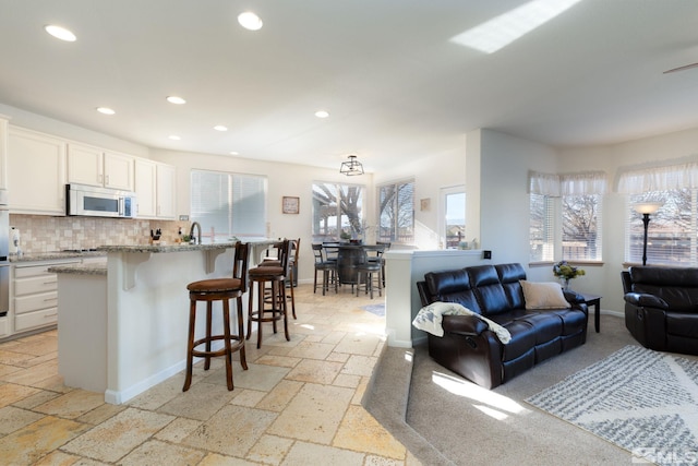 kitchen with backsplash, white cabinets, light stone countertops, an island with sink, and a kitchen bar