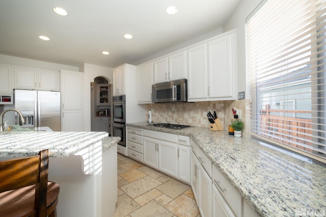 kitchen with tasteful backsplash, light stone counters, a breakfast bar, stainless steel appliances, and white cabinetry