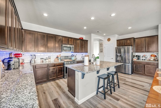 kitchen with light stone counters, backsplash, a textured ceiling, appliances with stainless steel finishes, and light wood-type flooring