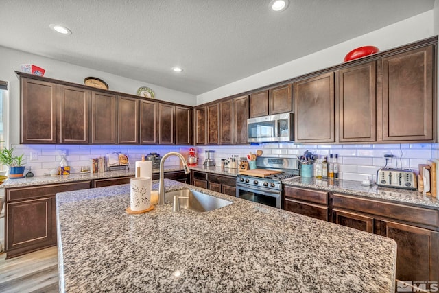 kitchen featuring sink, light wood-type flooring, light stone counters, dark brown cabinetry, and stainless steel appliances