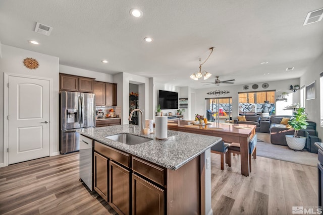 kitchen featuring ceiling fan, sink, stainless steel appliances, a center island with sink, and light wood-type flooring