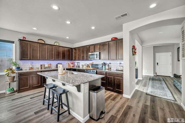 kitchen featuring light stone countertops, sink, stainless steel appliances, an island with sink, and light hardwood / wood-style floors