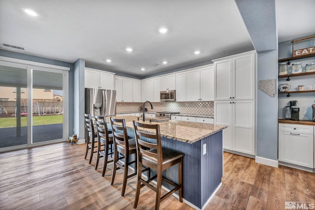 kitchen with white cabinets, light wood-type flooring, stainless steel appliances, and light stone countertops