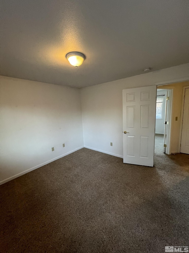 unfurnished room with a textured ceiling and dark carpet