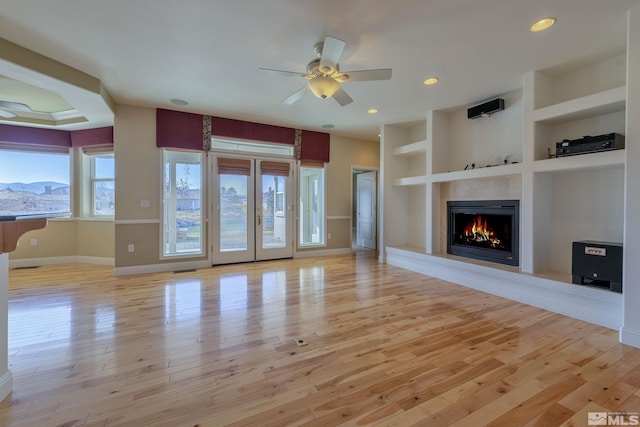 unfurnished living room with built in shelves, light hardwood / wood-style floors, and a wealth of natural light