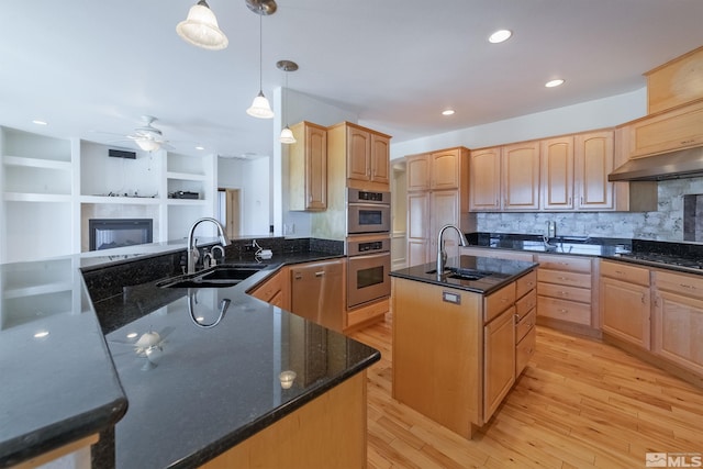 kitchen with sink, an island with sink, hanging light fixtures, and light hardwood / wood-style flooring