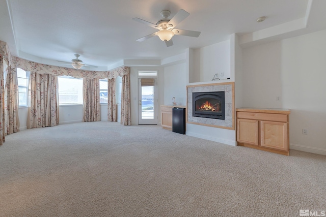 unfurnished living room with a tiled fireplace, light carpet, and ceiling fan