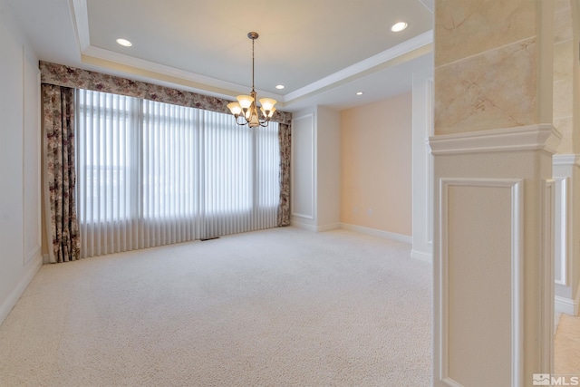 carpeted spare room featuring a raised ceiling, ornamental molding, and an inviting chandelier