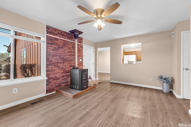 unfurnished living room featuring light hardwood / wood-style floors, a wood stove, and ceiling fan